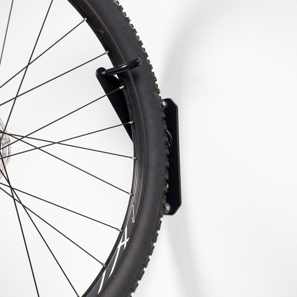 Bike hanging vertically on the PRx Single Bike Storage in a home garage gym
